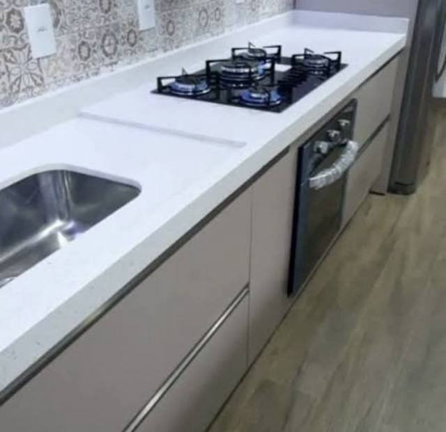 Bancada em pedra branca com cooktop e forno integrados.